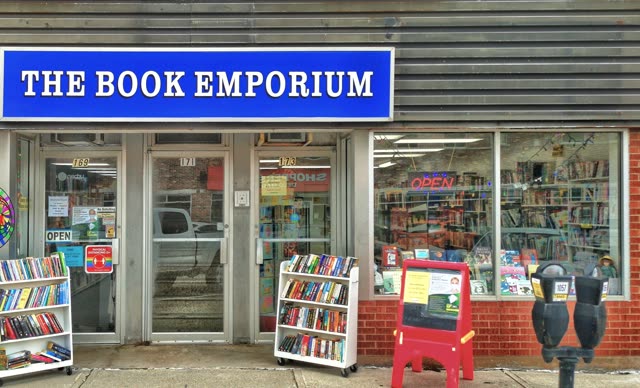 The Book Emporium on Queen Street: the blue shop sign, the door, wire book carts of paperbacks outside, and shelves of books visible through the window.